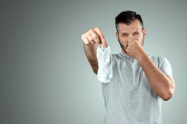 A young man holds his smelly socks and covers his nose with his hand