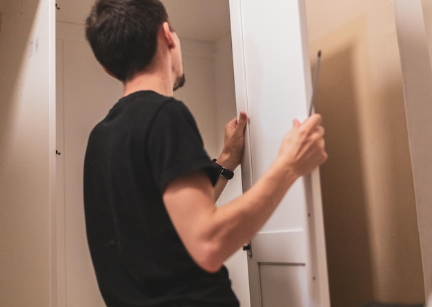 A young man holds the side door of a wardrobe