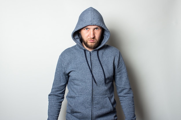 Young man in a hood with a serious, aggressive face against a light wall