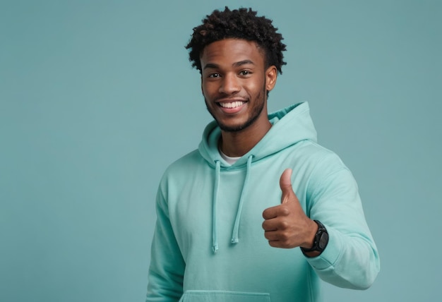 A young man in a hoodie smiling and giving a thumbs up looking comfortable and approachable in a