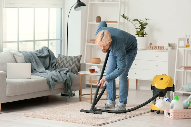 Young man hoovering carpet at home