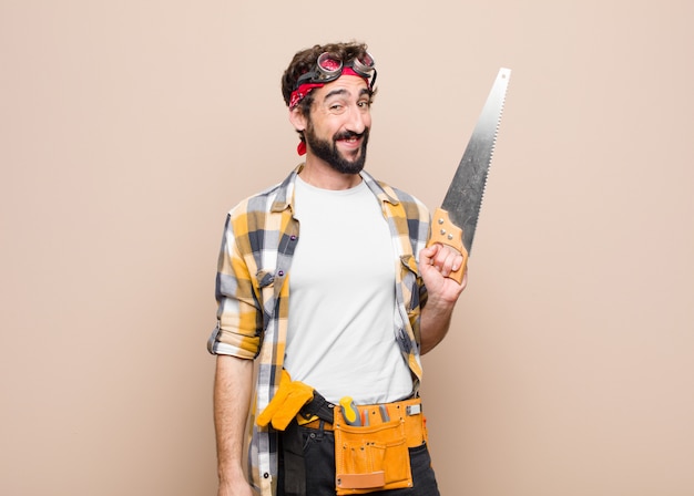 Young man housekeeper holding a saw against flat wall