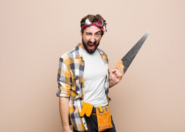 Young man housekeeper holding a saw on flat wall