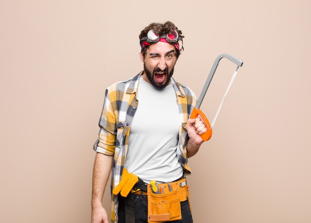 Photo young man housekeeper holding a saw on wall