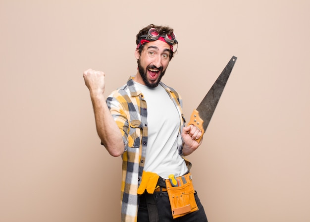 Young man housekeeper holding a saw on wall