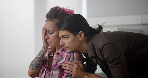 Young man hugging and comforting sad wife in wheelchair