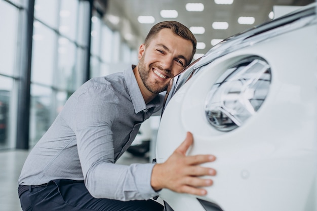 カーサロンで彼の新しい車を抱き締める若い男