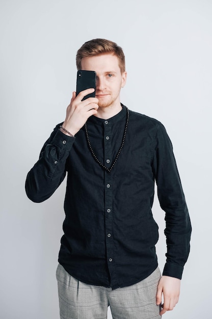 Фото Молодой человек в черной рубашке со смартфоном в руках на белом фоне