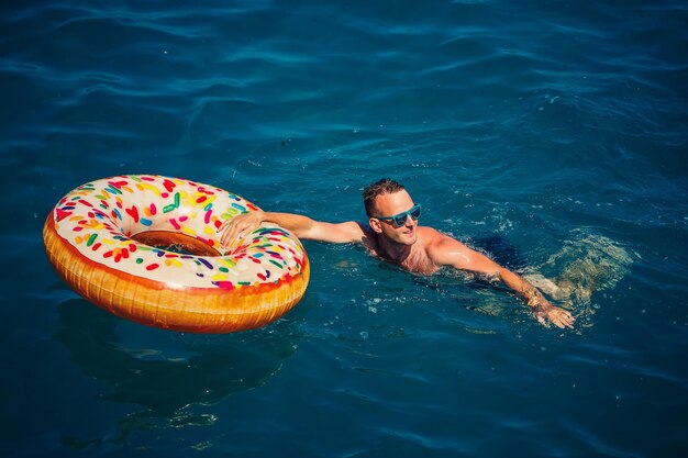 Молодой человек на надувном кольце в море отдыхает и плавает в солнечный день