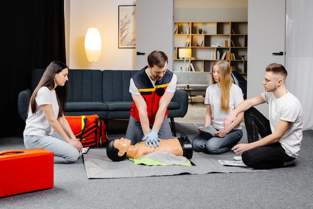 Young man instructor helping to make first aid heart compressions with dummy during the group training indoors