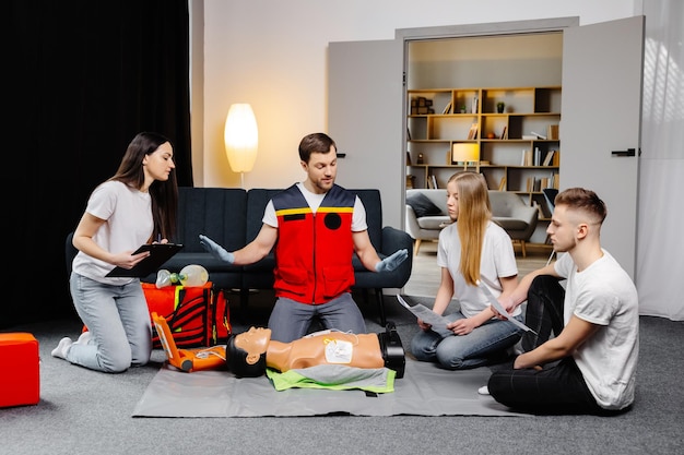 Young man instructor helping to make first aid heart compressions with dummy during the group training indoors