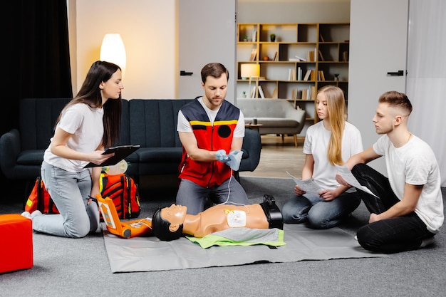 Young man instructor helping to make first aid heart compressions with dummy during the group training indoors