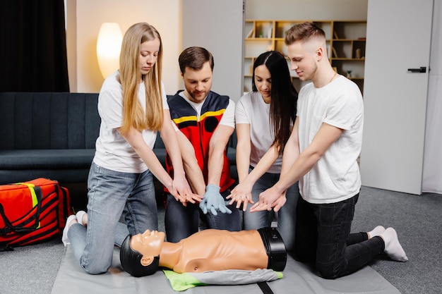 Young man instructor helping to make first aid heart compressions with dummy during the group training indoors