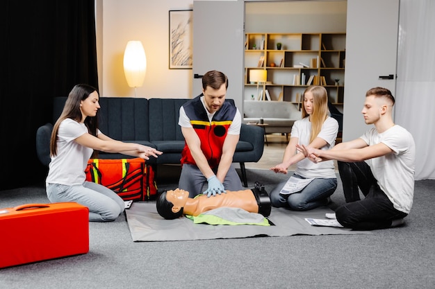 Young man instructor helping to make first aid heart compressions with dummy during the group training indoors