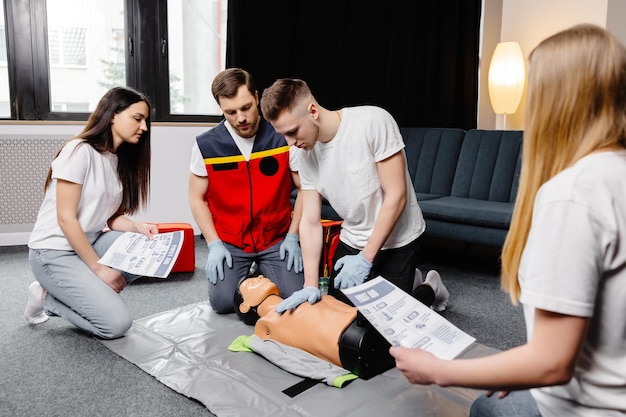 Young man instructor helping to make first aid heart compressions with dummy during the group training indoors