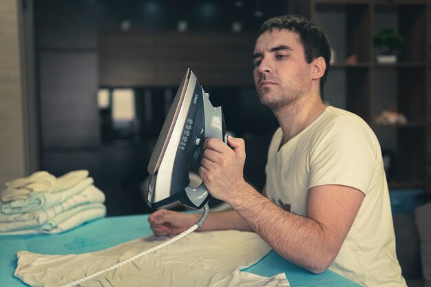 Young man irons his clothes at home against the background of the home interior