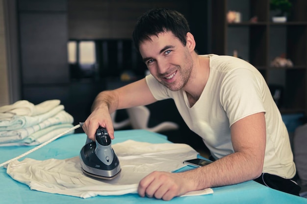 Young man irons his clothes at home against the background of the home interior