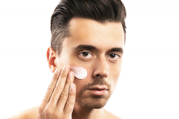 Young man is applying moisturizing cream on his face