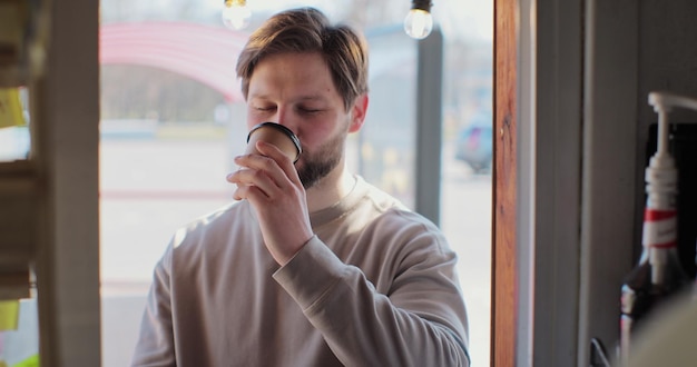 若い男は喫茶店で持ち帰り用のコーヒーを買い、スマートフォンで支払い、非接触型決済を行う現代のテクノロジーと銀行のコンセプト