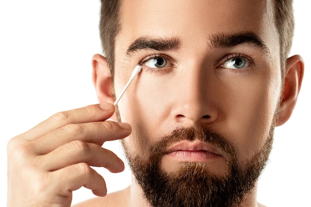 Young man is cleaning his eye with a cotton swab