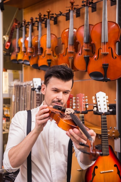 若い男は、音楽店でバイオリンを検討しています。