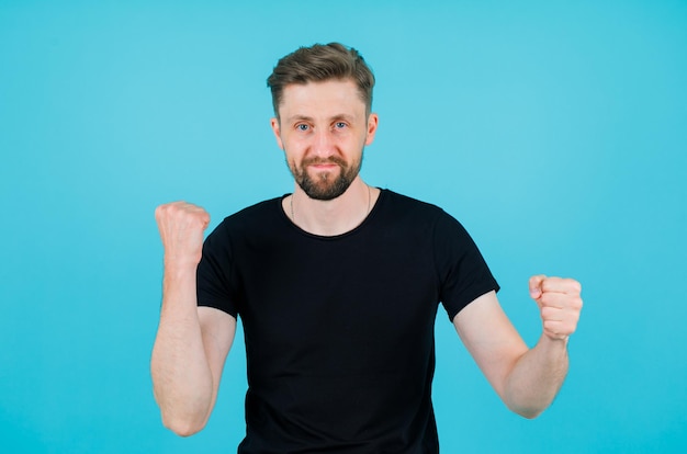 Young man is dancing by raising up his fists on blue background