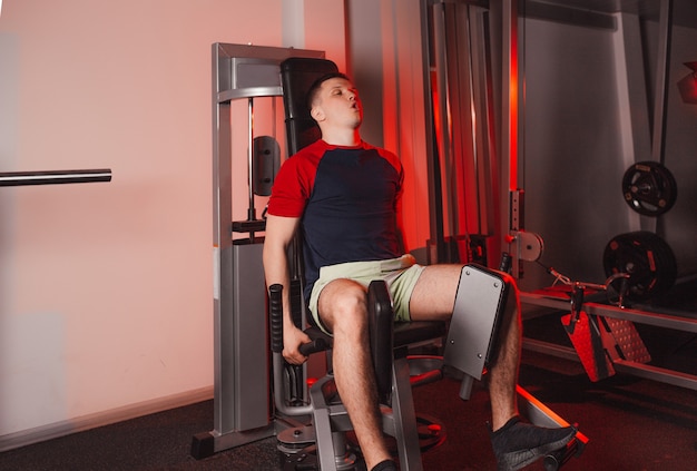 A young man is engaged in training his legs while sitting on a simulator in the gym. strength training