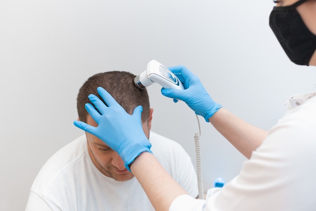 Photo a young man is examined with a trichoscope the condition of the scalp and hair follicles.