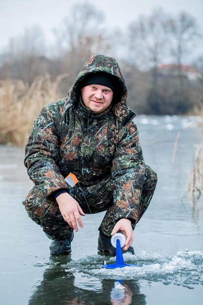 Молодой человек ловит рыбу из проруби на льду Зимняя рыбалка