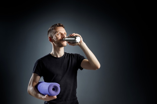 Young man is holding a fitness bottle and a fitness mat