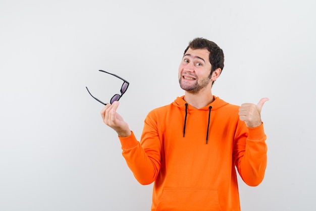 The young man is holding glasses and pointing back with thumb on white background