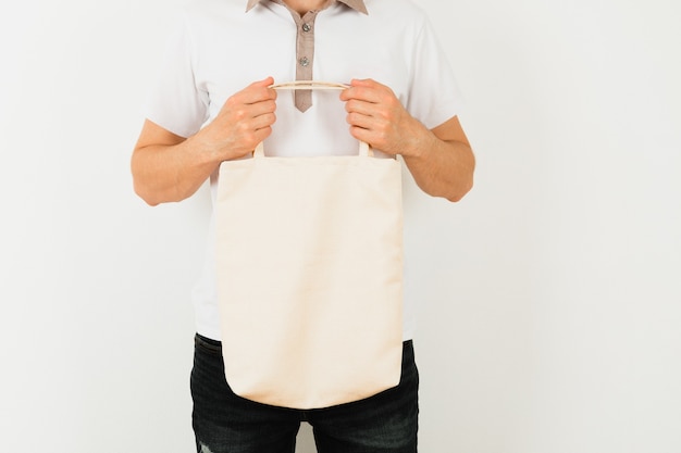 Young man is holding white textile eco bag on white