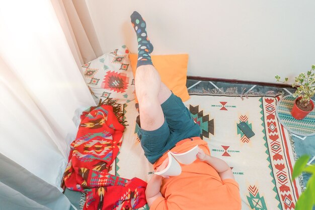 Young man is laying on a carpet and reading a bookc olorful socks colorful carpet