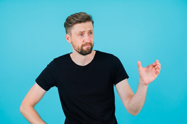 Young man is looking right and raising up his right hand on blue background