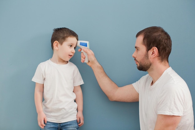 Young man is measuring body temperature of a toddler boy on a blue background