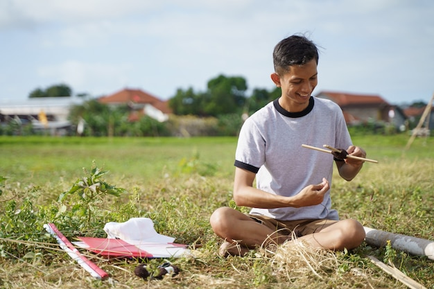 A young man is preparing a bamboo stick for a kite