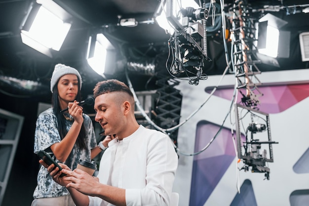 Young man is preparing for TV online broadcast Woman helps with make up