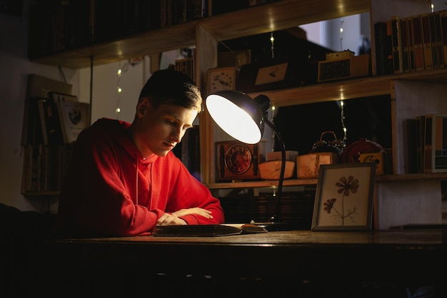 A young man is reading an old book in the library under a table lamp