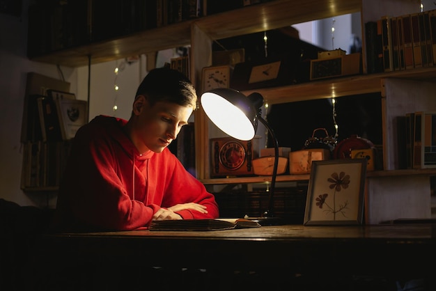 Photo a young man is reading an old book in the library under a table lamp