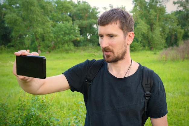 A young man is recording a video blog in the park on the phone