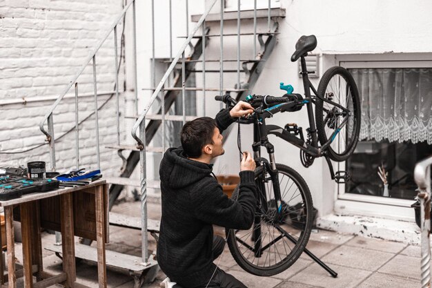 A young man is repairing a bicycle in the backyard of the house