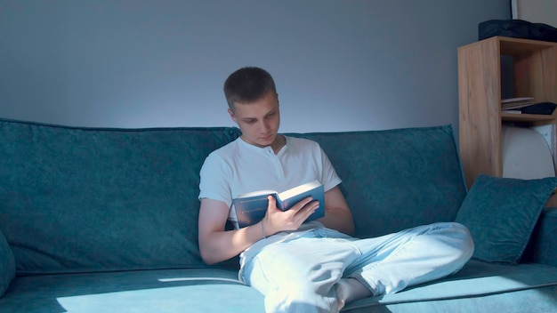 Молодой человек серьезно читает книгу в домашних СМИ красивый человек читает книгу сидит на диване в