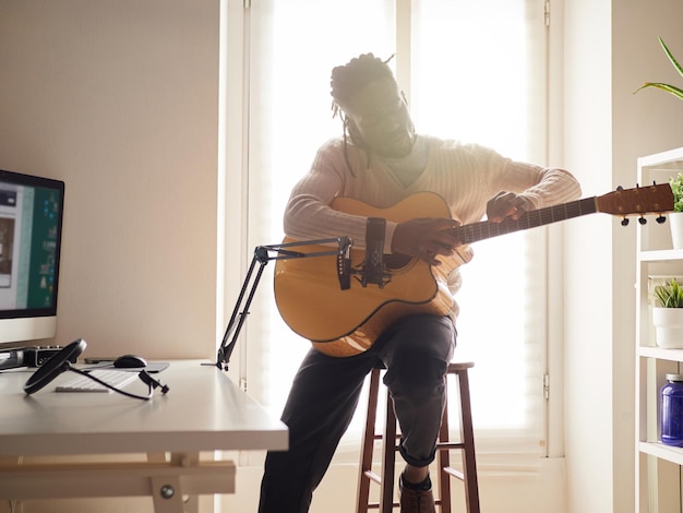 Young man is singing and playing guitar while making an audio recording at home