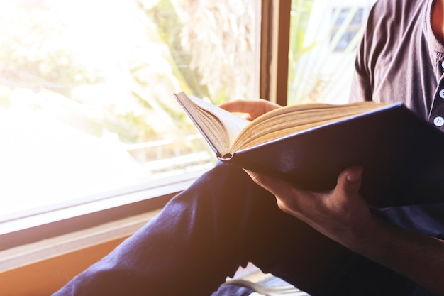 Young man is sitting reading in the window in the room 