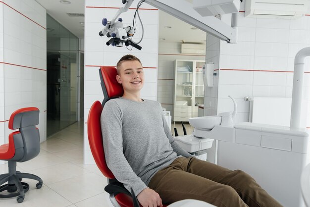 A young man is sitting in a red dental chair and smiling in
modern white dentistry treatment and prevention of caries from
youth modern dentistry and prosthetics