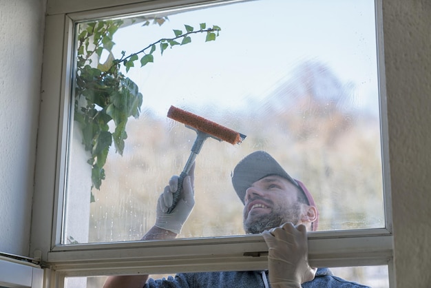 young man is using a rag and squeegee while cleaning windows. professional window cleaner