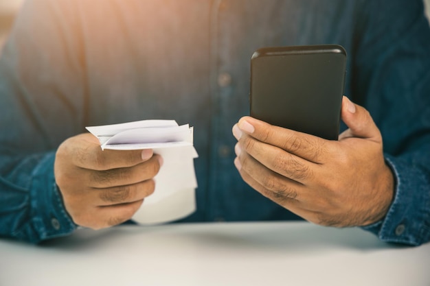 A young man is using a smartphone to scan the bill to calculate his income and expenses