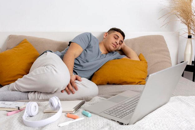 Young man is very tired after studying and fell asleep Man with casual clothes lying on the bed at home with laptop computer Using elearning platform Distance education Cosy interior Deadline