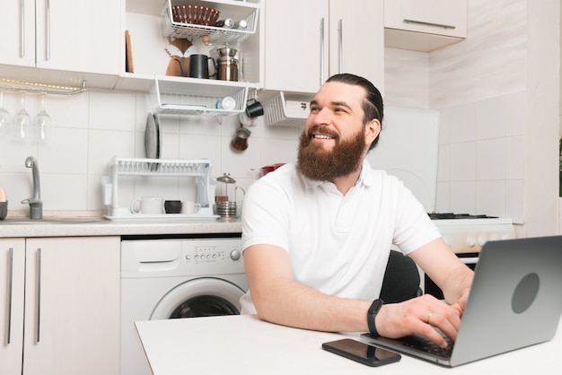 Young man is working at home at his laptop in the kitchen.