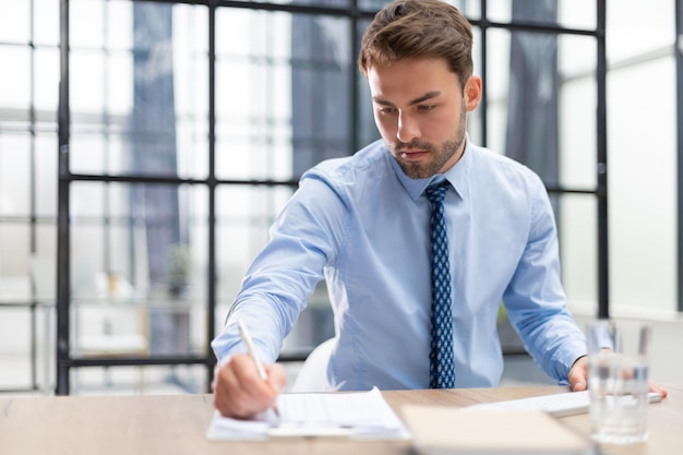 Young man is working with papers while sitting in the office Successful entrepreneur is studying documents with attentive and concentrated look